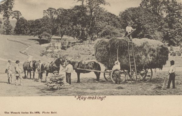 Postcard distributed by International Harvester Company of a photograph of a group of men loading bales of hay onto a horse-drawn wagon. Some of the men appear to be well-dressed. Original caption below the photograph reads: "Hay-making."
