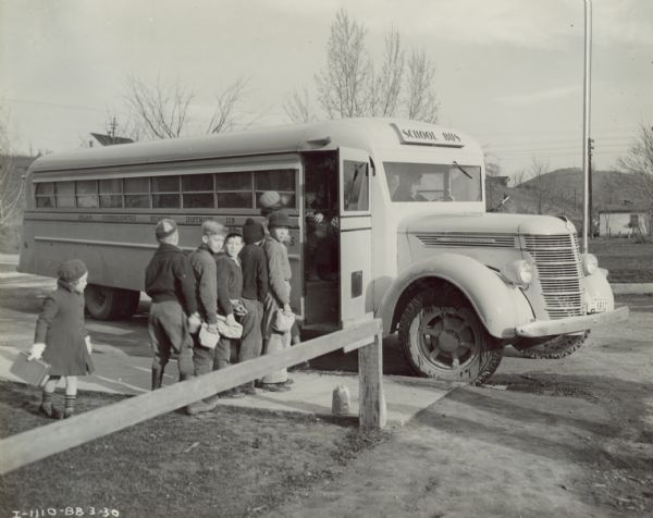 Students waiting in line to board an International D-40 school bus at a school. The 60 passenger bus was equipped with a 235-inch wheel base and an Olympian Body.
