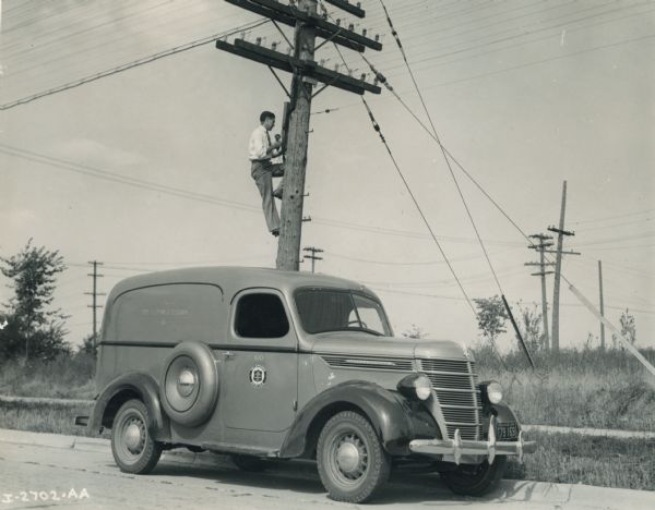 International D-2 truck used by the Home and Telegraph Company. A man on a telephone pole is dressed in a suit and tie. The D-2 truck had a 113-inch wheel base.