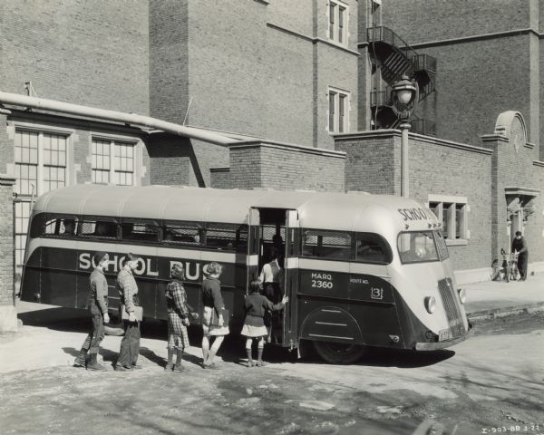 Children standing in line, boarding an International D-300 bus near what appears to be a school buiding. This bus was equipped with 165" Hicks body.
