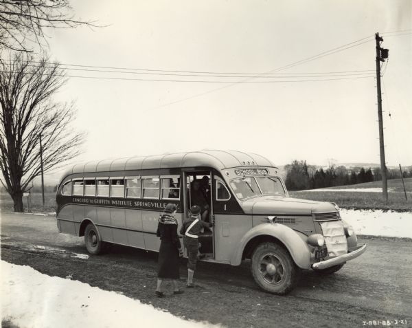 Two students boarding an International D-50 bus. This bus was equipped with a 235-inch wheel base and a Penn Fan Deluxe, 24 foot body.