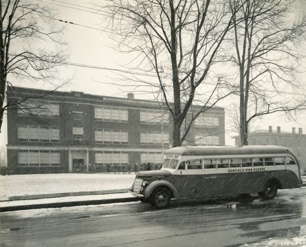 International D-40 bus parked outside of Oakfield High School on a snowy day. Students appear to be filing out of school. This bus was equipped with a 235-inch wheel base and Rex-Watcon 49 Passenger body.