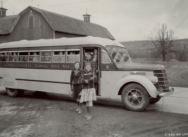 Smiling children disembark from an International D-Line school bus with a Penn Fan body. The bus is stopped near a barn.