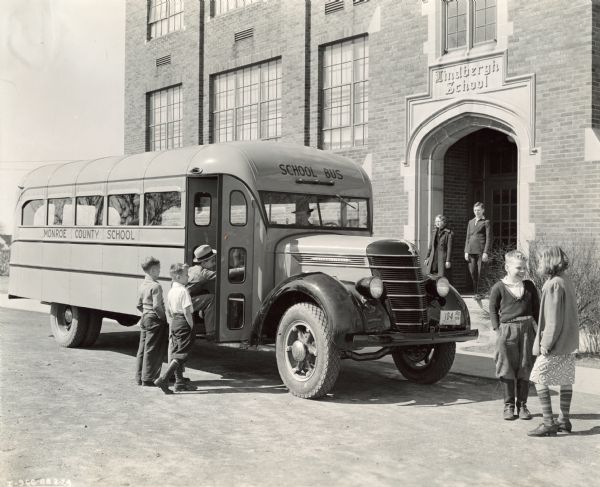 Students boarding an International D-30 bus at Lindbergh School in Monroe County. One of the boys and the bus driver are wearing brimmed hats.