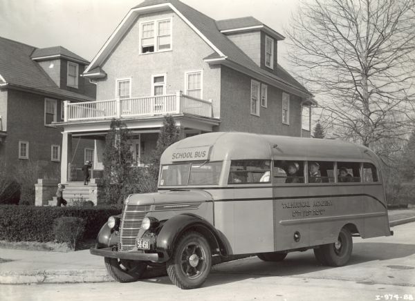 International D-30 bus with a Bender body drops off two students from the Talmudical Academy. The bus is parked in front of a house in a residential neighborhood. All the students appear to be in uniform.