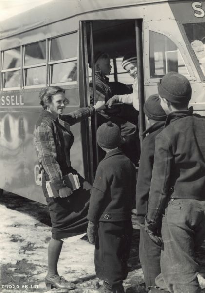 Students boarding an International D-40 school bus. This bus was equipped with a Rex-Watson body and a 215-inch wheel base, and seated 49 passengers. The students appear to be wearing winter clothing: jackets, hats and mittens.