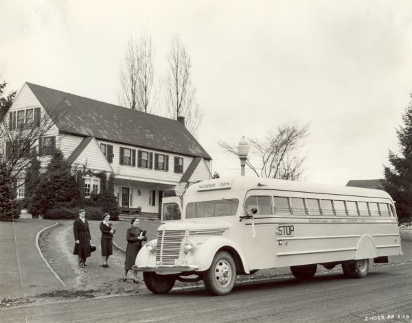 Three students boarding an International D-40 bus in a residential neighborhood with a large house in the background. The bus was equipped with a Cascadian body, 252-inch wheel base, and seated 60 passengers.
