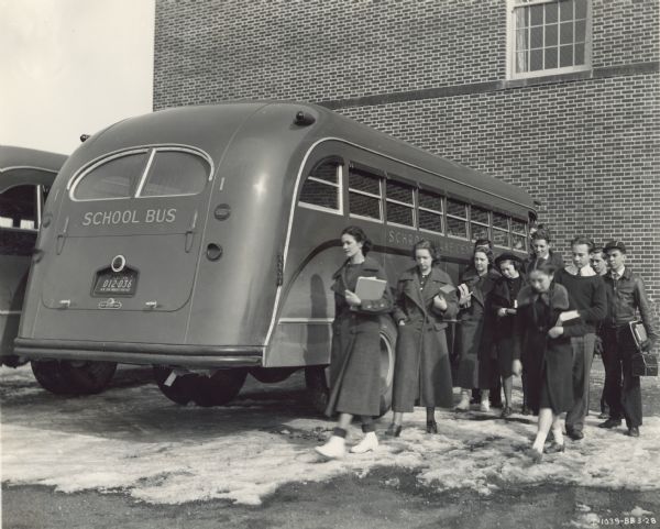 Students outside of an International DS-50 school bus at Schroon Lake Central School. The students are dressed for winter. The bus was equipped with a Rex-Watson body, 215-inch wheel base, and seated 49 passengers.