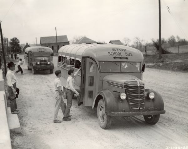 An International Model D-30 picking up students on a rural road. This bus was equipped with a 191-inch wheel base. There is a similar bus in the background.
