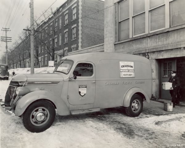 International D-15 truck parked near a loading dock on a snow-covered city street. The truck was one of three operated by Canadian Pacific Express in Montreal and Quebec, Canada. A man stands behind the truck near a building holding boxes.