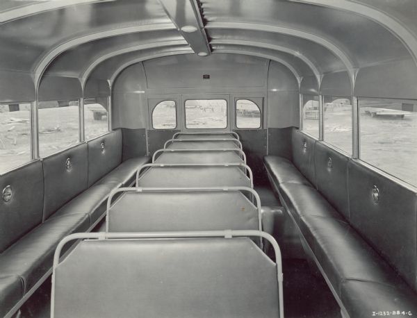Interior view from front of "seating plan A" for an International bus with a Hicks body. Two bench-style rows run along under the windows facing the center of the bus, with one center row of seats down the middle facing the front of the bus.