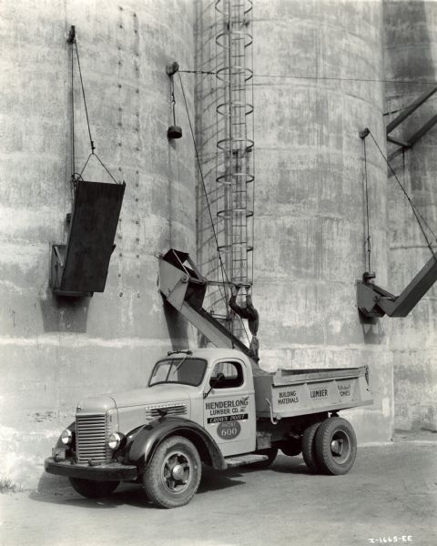 One of 18 International Model K-6 trucks owned and operated by Henderlong Lumber Company, Inc. A worker is operating one of three dump mechanisms to fill the bed of the truck from large storage tanks.