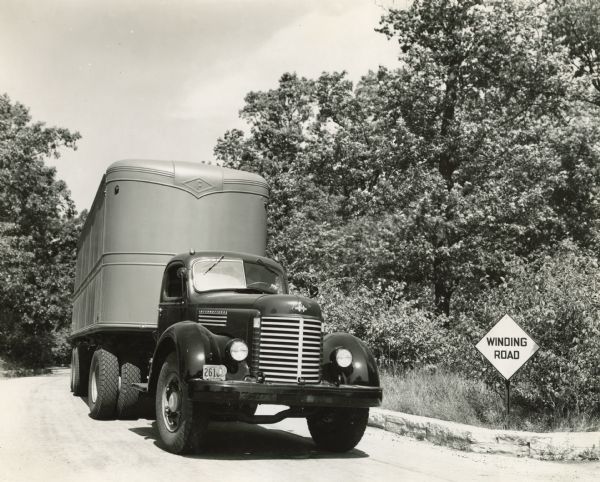 International D-Line truck with semi-trailer, driving along a winding road in a wooded area.