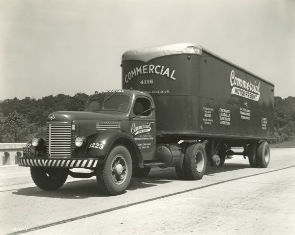 International truck with a semi-trailer owned by Commercial Motor Freight, Inc. of Indiana. The truck appears to be parked on a highway with a concrete railing.