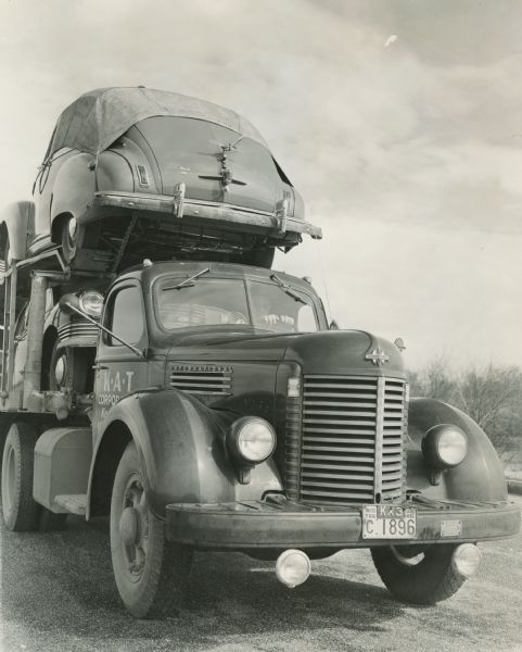 A man sits behind the steering wheel of an International truck utilized by K*A*T Corporation for multi-automobile hauling.
