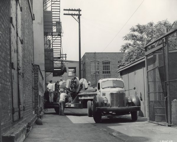 Men unloading machinery from an International KB-10 truck. The original caption reads, "An International KB-10 with Rodgers body and Braden winch owned by the Shea-Matson Machinery Movers of Chicago, Illinois. The truck is shown unloading five punch presses, two printing presses and one paper press at the Eversharp plant in Chicago."