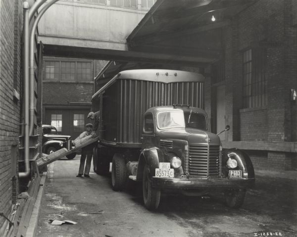 International K-8 truck and trailer owned by Jack Marsh Motor Transport. Two men are loading or unloading the truck in an urban alley. Original caption reads: "This unit makes three round trips a week between Toronto and Montreal [Canada]."