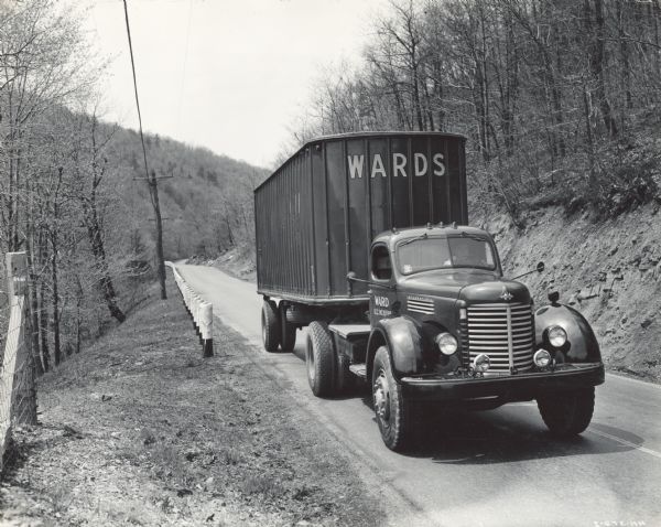 International KS-11 truck and trailer (semi-truck) traveling the highway leading out of Altoona. The truck was operated by Ward Trucking. Original caption reads: "In traveling these mountainous roads the new KS-11 trucks pulling the full-load 28-foot trailers are proving most economical hauling units, averaging around 5 miles to the gallon."
