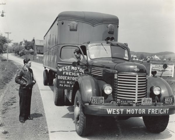 International KR-11 truck with semi-trailer (semi-truck) parked on a rural road. The truck was owned and operated by West Motor Freight of Boyertown, Pennsylvania. According to the original caption, the scene shows a "young, keen-looking Winfield West, head of the concern, talking to one of his drivers."