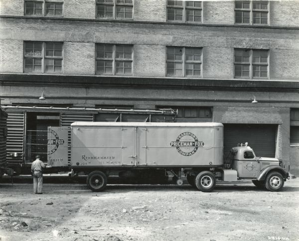 International KR-11 truck with refrigerated semi-trailer (semi truck) parked next to a box car near a warehouse building. Original caption reads: "Meat and other perishable foods are everyday necessities, of course, but when they go to army camps the hauling of these foods by truck certainly comes under the designation of war business. In the [photograph] is one of the two KR-11 International motor trucks recently added to the fleet of the Priceman-Fox Transport Company of Philadelphia which specializes in hauling of perishable foods... The new KR-11 shown is strikingly finished in orange and blue. The trailer is 26 feet long and has a refrigerator body, refrigeration being provided with dry ice... The average trailer load is 25,000 pounds."
