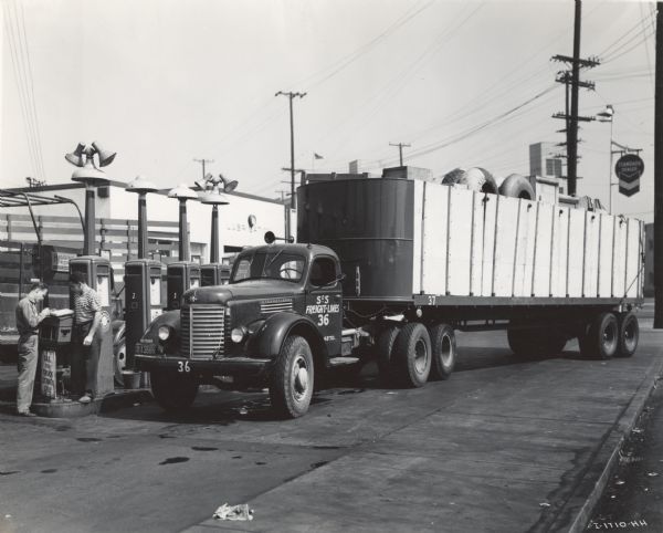 International KR-11 truck and semi-trailer (semi-truck) parked near gas pumps at a service station. Original caption: "The truck shown is [this picture] at a filling station in Los Angeles is one of four new KR-11 Internationals added to the fleet of 25 units operated by S & S Freight Lines of Oakland, California. It travels loaded both ways between Sacramento, Stockton, and Los Angeles for a total round trip of some 800 miles. The stake body is 35 feet long, 8 feet wide, and 6 feet high."
