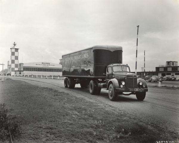 Man driving an International KR-11 truck with semi-trailer at the Billings Municipal Airport. The truck was operated by Northwest Freight Lines. Original caption reads: "A recent purchase obtained through ODT release is the KR-11 International motor truck shown... in front of Billings Municipal Airport... The Refer-van trailer is 32 feet long, 8 feet wide and 7 feet high.