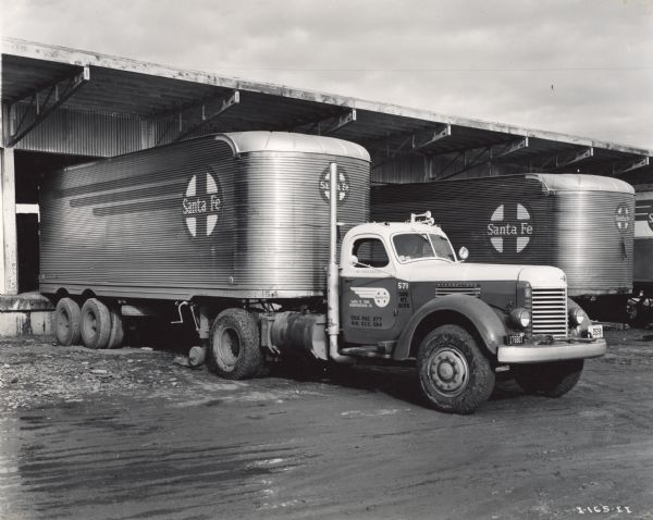 International KRD-11 truck with semi-trailer backed up to a loading dock. Original caption reads: "The Santa Fe Trail Company of Albuquerque, New Mexico, recently placed in service six Internationals KRD-11 Diesel motor trucks, one of which is shown at the company's Albuquerque terminal. The company operates a fleet of 64 units in intercity bus and truck service... The truck shown was purchased September 28, 1944, and its total mileage at the end of the year was 60,000 miles. The van-type trailer is 28 feet long, 8 feet wide, and 11 feet 8 inches high."