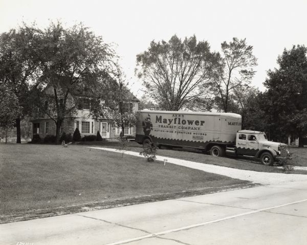 View across street of an International K-8 truck in a residential driveway. Original caption reads: "the new type units being operated by Aero Mayflower Transit Company. The truck shown is a Model K-8 with a sleeper cab and semi-trailer van body. Photographs were made in Indianapolis."