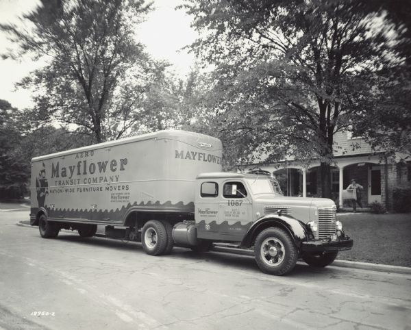 International KB-7 with sleeper cab and semi-trailer owned by Aero Mayflower Transit Company, Indianapolis, Indiana. View from street shows a man on the lawn of a house loading furniture into the trailer.