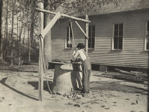 Boy retrieves water from a school well. Original caption reads: "This Old fashioned well, at Sheffield School near Union City, Tenn. is typical of the entire South, there being but few places equipped with modern appliances such as pumps, sinks, etc. In a three weeks tour of Tennessee, Mississippi, Arkansas but few places were visited where they had pumps in the wells. Drawing water by this crude method saps the strength of many southern women--And most of all such wells as the one portrayed here permits surface water to get in and in many instances spreads disease."