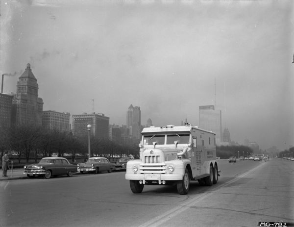 International RD-190 (?) truck with an armored body, operated by the Brinks Express Company on Lake Shore Drive. Parked cars and a pedestrian are in the background.