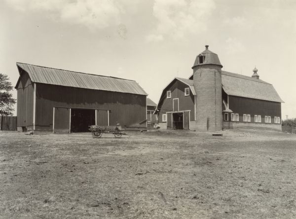Two barns, a silo, and a wagon on a farm.