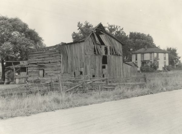 View across road of a deteriorating barn and a few sheds. In the background is a young child standing in the yard of a farmhouse. Original caption reads, "Fairly good looking house spoiled by a tumble down barn and sheds." :he photograph was taken on Dixie Highway.