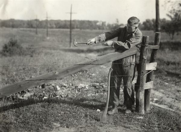 Man tightening a wire fence. Original caption reads: "R.A. Hayne tightening a wire fence on the John Esch farm."