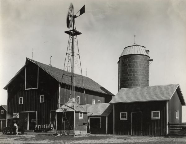 Farm buildings, including a barn, silo and windmill. There is a man dressed in overalls and a wide-brimmed hat standing near an automobile. Caption reads: "Noah Schwunk, Sterling, Ill."