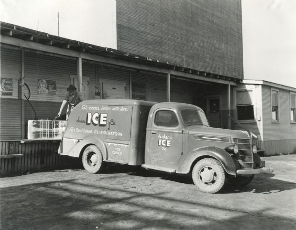 A man uses tongs to load blocks of ice from a loading dock onto the back of an International D-15 truck owned by the Salem Ice Company. The text on the truck reads: "It keeps better with Ice! Salem Ice Co. Air Conditioned Refrigerators. Ice Cubes."