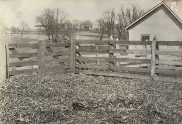 View of a wooden fence with gate next to a small house. Original caption: "Stout gate & fences. Litter covered barnyard to keep it dry & from being trampled."