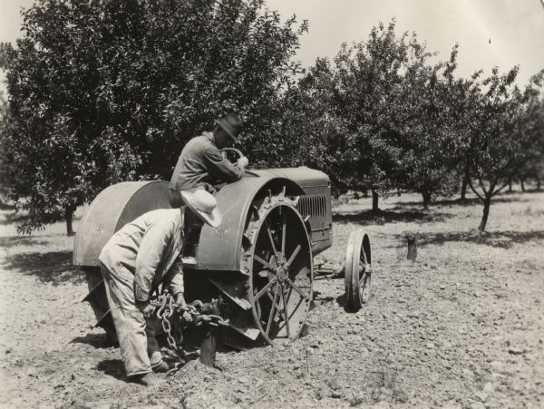 Two men using what appears to be a McCormick-Deering 10-20 tractor to "pull stumps" in an orchard on the R.R. Robertson farm.