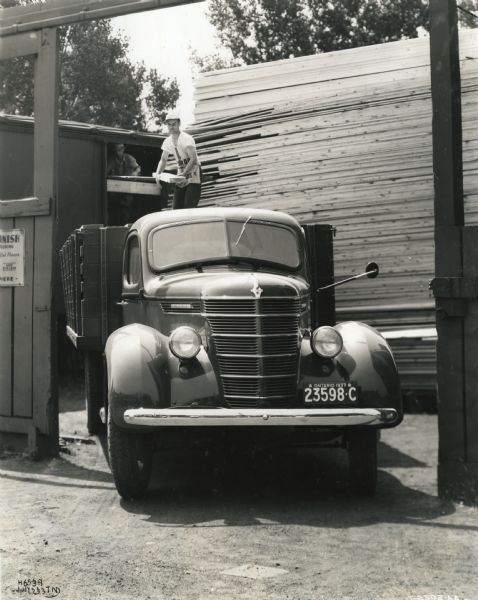 Two men from the Alliance Lumber Company Limited load lumber onto the bed of an International D-35 truck. The truck features a 179-inch wheelbase.