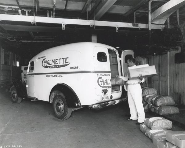 A man loads boxes and packages into the back of an International D-2 truck owned by the Chalmette Laundry division of the Crescent City Laundries, Incorporated.