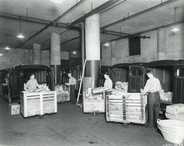 Four employees of Sibley, Lindsay, and Curr Company department store load wrapped packages into the backs of a fleet of eight International Model D-15 trucks.