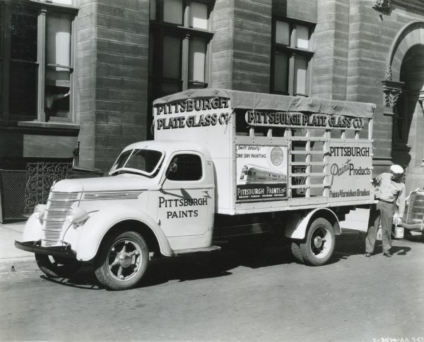 A man unloads buckets of paint from the back of an International D-30 truck owned by Pittsburgh Paint Products.