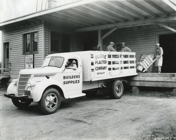 Men load bags of plaster from a loading dock onto the back of an International D-30 truck owned by the Globe Plaster Company.