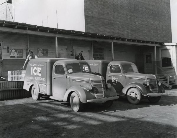 Two men load blocks of ice from a loading dock onto the backs of International D-2 and D-15 trucks owned by the Salem Ice Company.