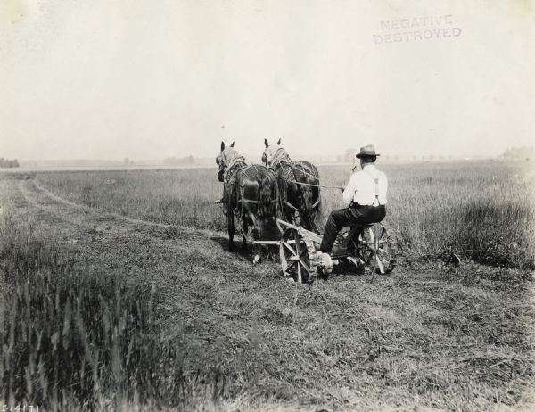 Man in a field operating a horse-drawn mower.