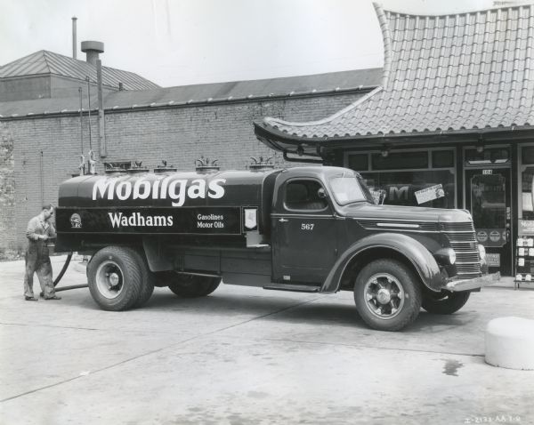 A man loads the rear of an International D-50 truck owned by Mobilgas while parked outside what appears to be a service station.