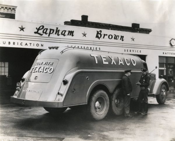 Two men stand beside an International D-346-F truck owned by Texaco. The truck is parked outside Lapham Brown Texaco service station.