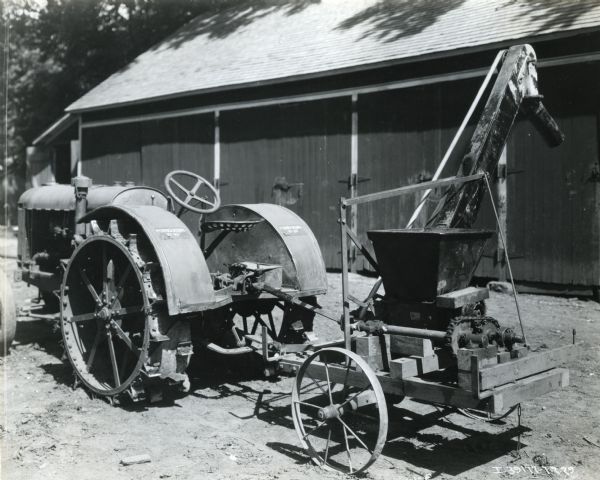 A McCormick-Deering 10-20 tractor attached to a corn sheller stands in a farmyard in front of a barn.
