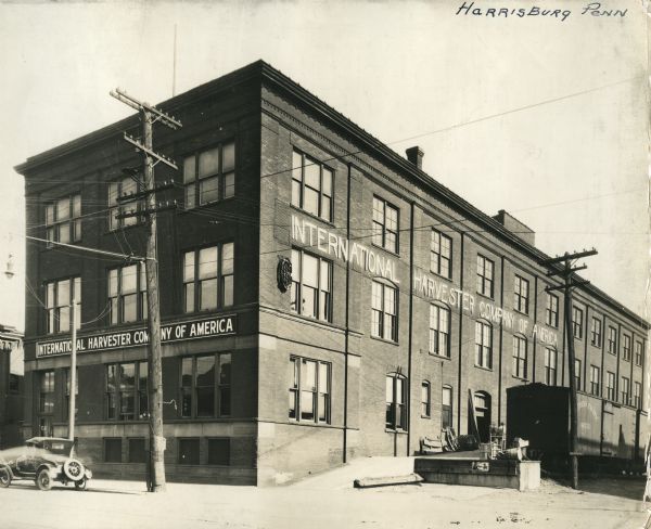 Exterior view of an International Harvester Company branch building. A train is parked alongside the building next to a loading dock.