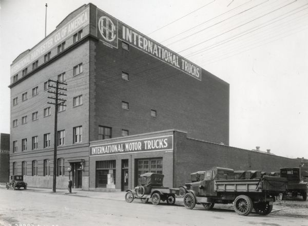 Exterior view of an International Harvester motor truck branch house.  Several trucks and automobiles are parked along the curb in front of the building.